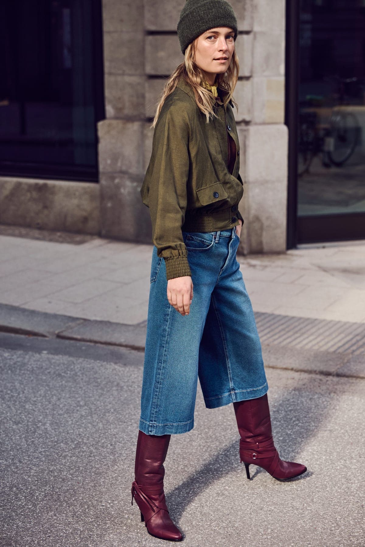 Woman in wide-leg NEFLYX jeans and burgundy boots crossing a city street